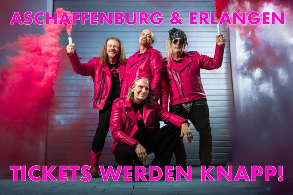 J.B.O. Band in pinken Jacken mit Rauch im Hintergrund.